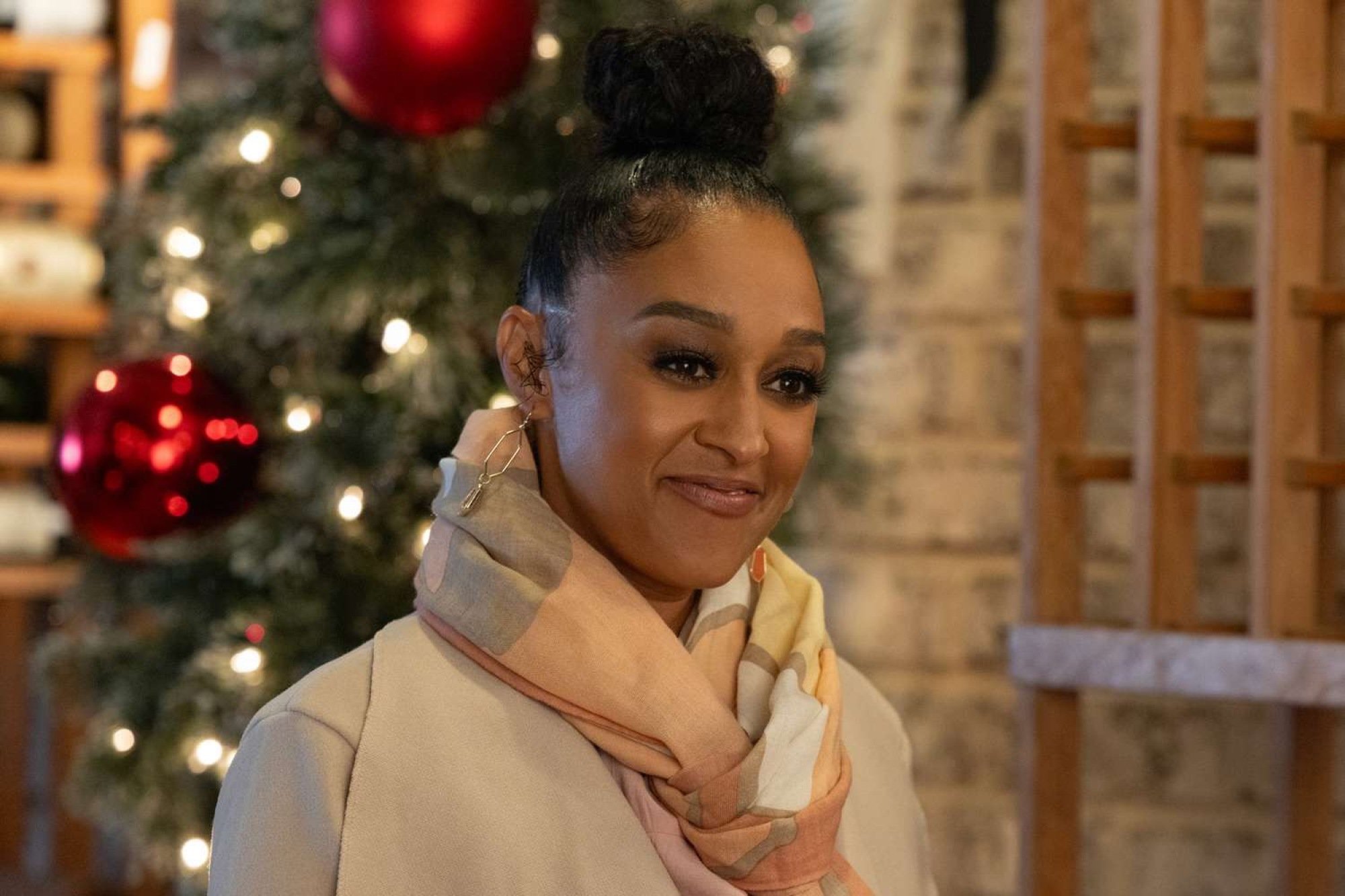 A woman in a jacket smiles in front of a Christmas tree.