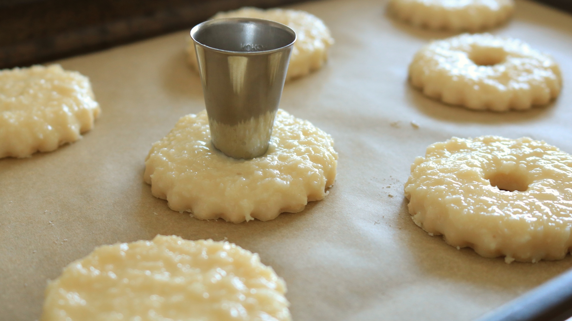 A metal piping tip cutting a small hole out of cookies on a sheet tray.