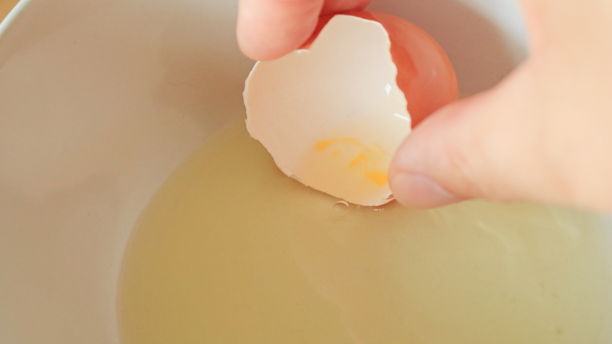 An egg shell scooping up egg yolks in a bowl of whites.