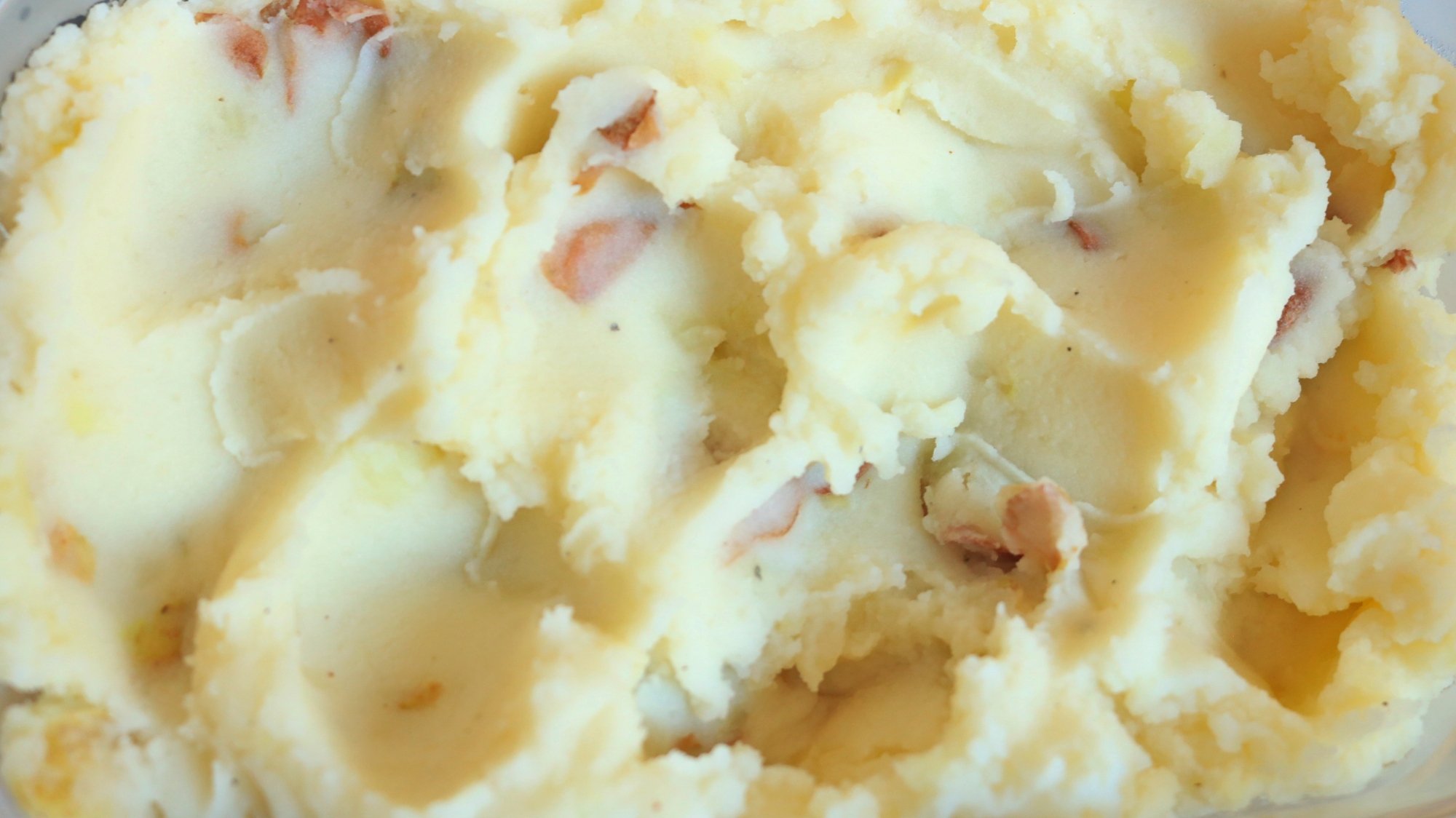 Close-up image of fluffy mashed potatoes with red potato peels.