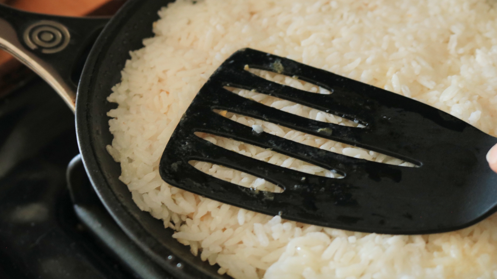 Spatula pressing rice into a frying pan.